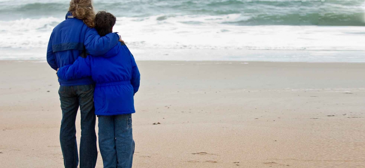 Hur ska vi bearbeta att pappa tog sitt liv? Bild föreställer två personer som står med ryggen mot kameran, vid en strand där vågor sköljer in över sanden