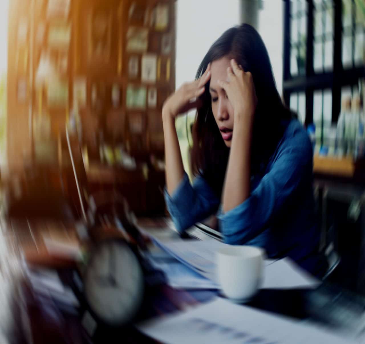 Artikel Kan man bota paniksyndrom. Bild visar en kvinna som sitter i ett rum och lutar huvudet i sina händer. Miljön runt om är suddig för att illustrera känslan av stress
