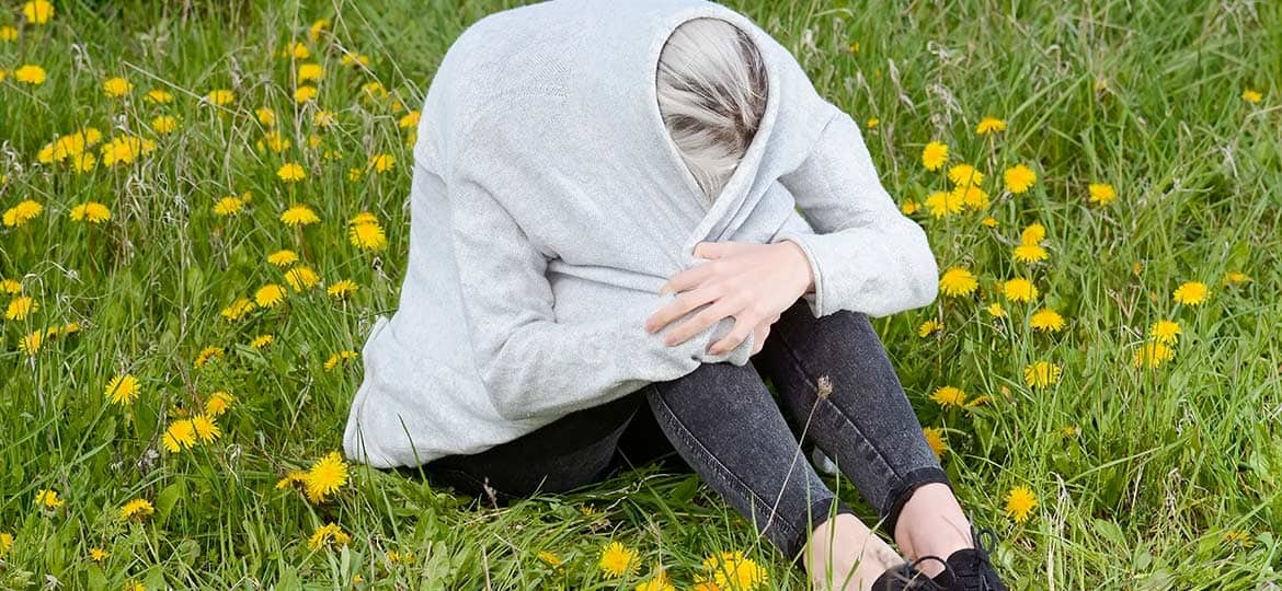 Kan man bli deppig av vårkänslor? En person sitter på en gräsmatta som är täckt av maskrosor