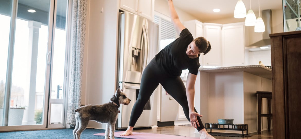 Kvinna gör yogaövning i sitt hem med sällskap av en liten hund