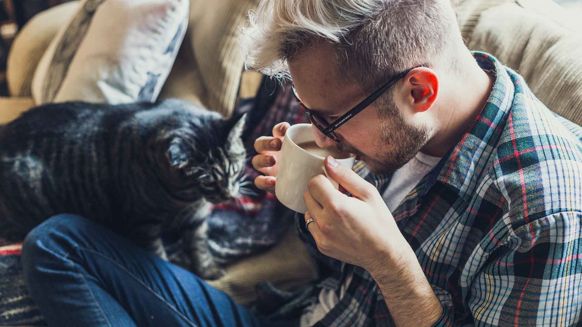 Har du svårt att göra en förändring? Bild på en man som sitter i sin soffa med en kopp kaffe med sällskap av en katt